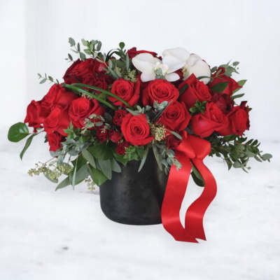 Low black vase of red roses with white orchids and a red ribbon bow