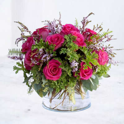 Pink roses arranged in a clear glass vase with greenery and small filler flowers
