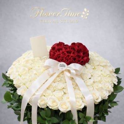 Heart-shaped red and white rose arrangement in a white basket with ribbon