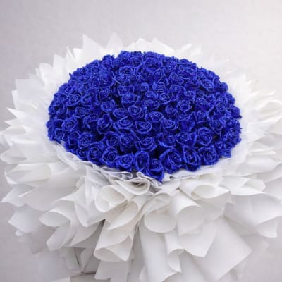 Blue rose bouquet with white wrapping in a pedestal vase