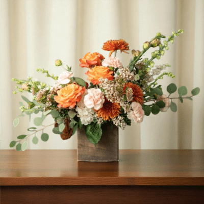Orange and blush floral arrangement in a wooden vase