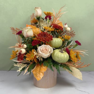 Autumn floral arrangement with roses, chrysanthemums, and small pumpkins in a vase