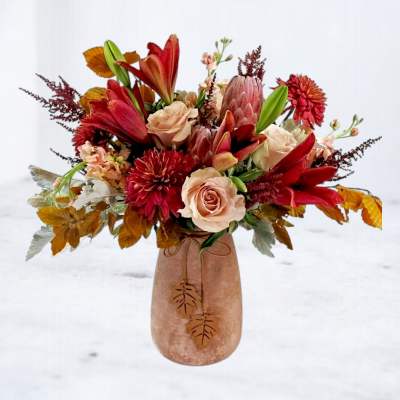 Autumn bouquet of red lilies and pale roses in a blush vase