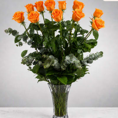 Orange roses arranged in a clear glass vase with mixed greenery