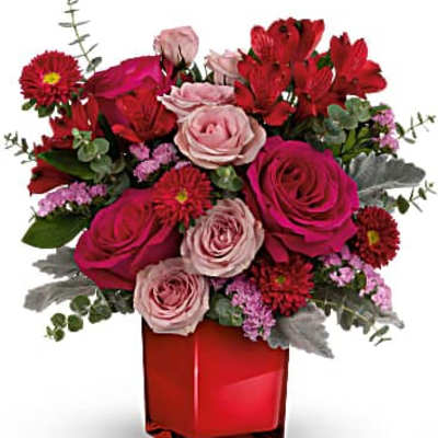 Red and pink mixed flower arrangement in a red square vase