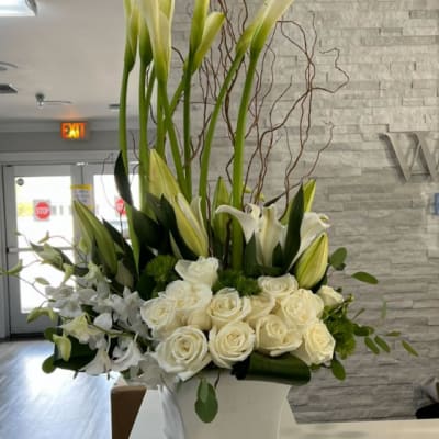Tall white floral arrangement with roses and lilies in a square vase
