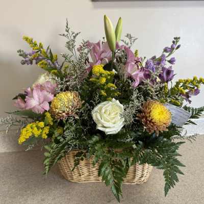 Mixed bouquet in a wicker basket with pink lilies, white roses, and yellow flowers