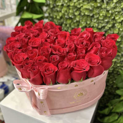 Heart-shaped pink hatbox filled with tightly packed red roses and tied with a pink ribbon