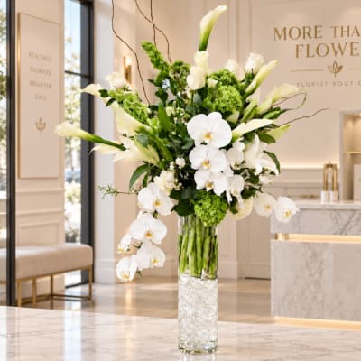 White orchids and green blooms arranged in a tall glass vase