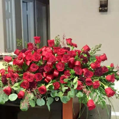 Large spray of red roses with dark red blooms and red ribbon arranged in a low, wide display