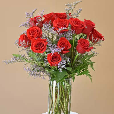 Red roses arranged in a clear glass vase with purple filler flowers