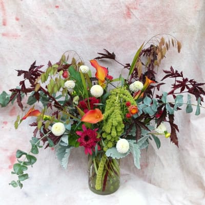 Mixed floral arrangement in a glass vase with orange calla lilies and white pom flowers