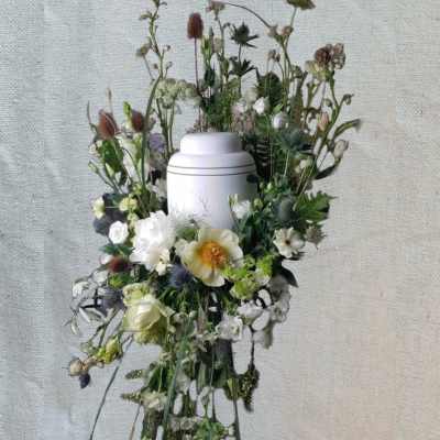 White urn surrounded by a loose floral wreath with white and pale green blooms