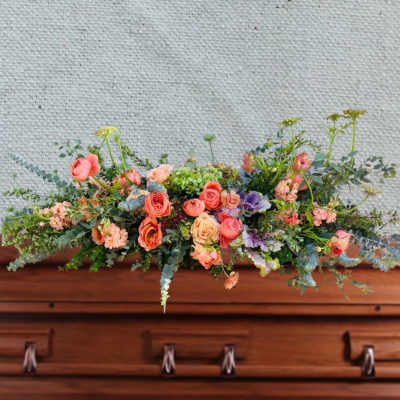 Low floral arrangement with peach and pink roses on a wooden casket