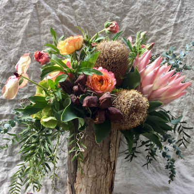 Mixed bouquet with pink protea, roses, and greenery in a rustic wood vase