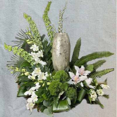 White orchids and green tropical foliage arranged around a tall metallic vase
