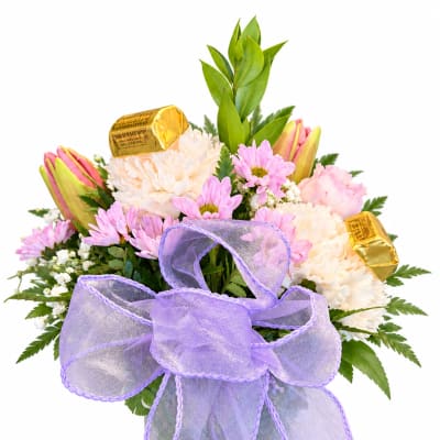 Pink and white bouquet in a glass vase with a purple bow and candy bars