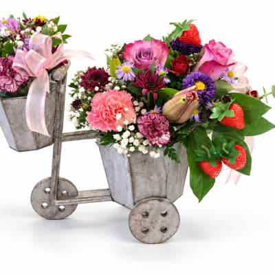 Two flower-filled metal buckets on a small cart with pink ribbons