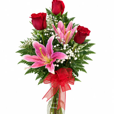 Red roses and pink lilies in a clear glass vase with a red bow