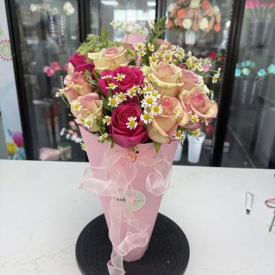 Pink and cream roses with small white daisies in a pink cone wrap
