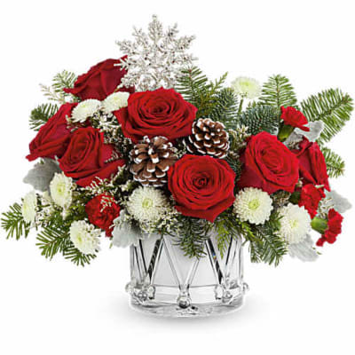 Red roses and white flowers arranged in a clear glass vase with pinecones