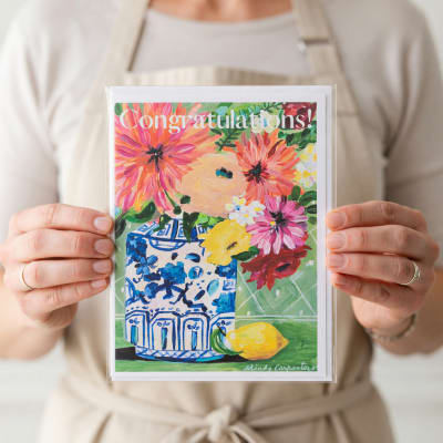 Person holding a floral congratulations card with a painted vase and flowers