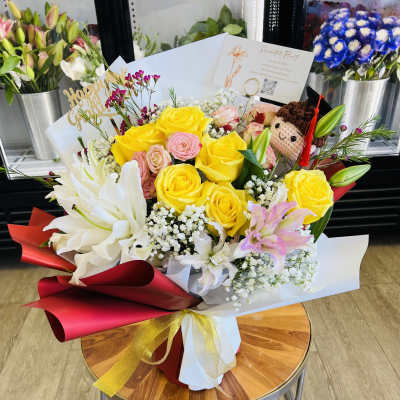 Bouquet of yellow and pink roses with white lilies and a small plush doll