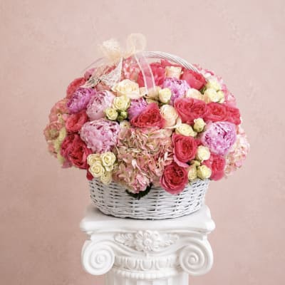 Basket of pink and cream roses with hydrangeas and a ribbon bow