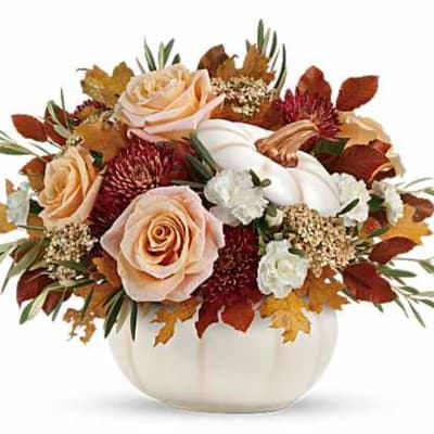 Peach roses and white flowers in a white pumpkin vase with autumn leaves
