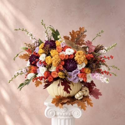 Colorful floral arrangement in a pumpkin vase with autumn leaves