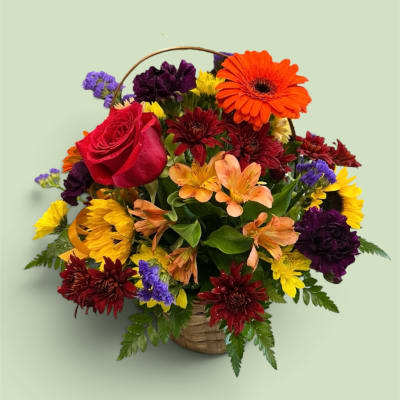 Mixed bouquet in a woven basket with a red rose and bright gerbera daisies