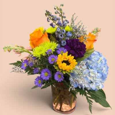 Colorful mixed bouquet in a glass vase with sunflowers, roses, and hydrangea