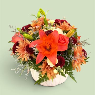 Orange lily and mixed autumn flowers in a white pumpkin vase