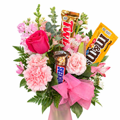 Pink floral bouquet in a frosted vase with candy bars and a pink bow