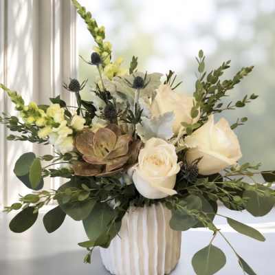 White roses and snapdragons in a ribbed vase with eucalyptus and succulents