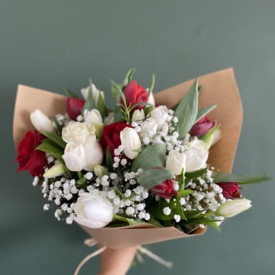 Handheld bouquet of red and white tulips wrapped in brown paper