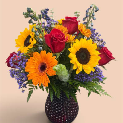Mixed bouquet of sunflowers, red roses, and orange gerbera daisies in a dark vase