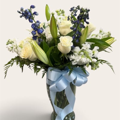 White roses and lilies with blue flowers in a glass vase tied with a blue ribbon