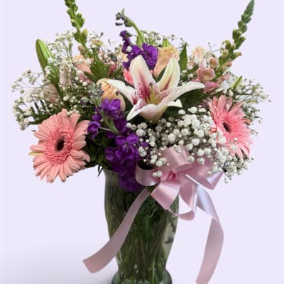 Mixed bouquet of pink and purple flowers in a glass vase with a pink ribbon