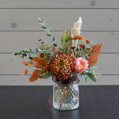 Orange and pink floral arrangement in a glass vase with a ribbon
