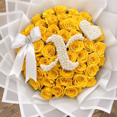 Bouquet of yellow roses with white floral heart accents and a white ribbon