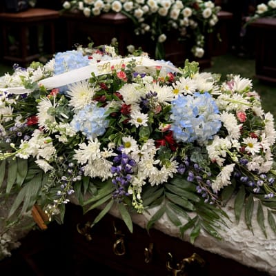 Large white floral casket spray with blue hydrangeas and purple accents