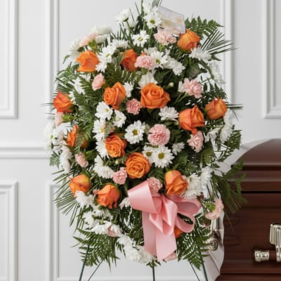 Orange roses and white daisies in a funeral spray with a pink ribbon