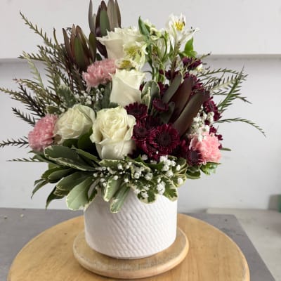 Mixed bouquet of white roses, pink carnations, and burgundy blooms in a white vase