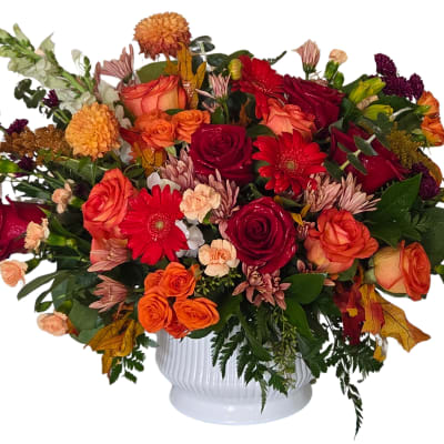 Mixed bouquet of red, orange, and peach flowers in a white vase
