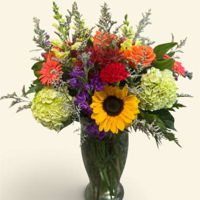 Colorful mixed bouquet in a tall glass vase with a sunflower and hydrangeas