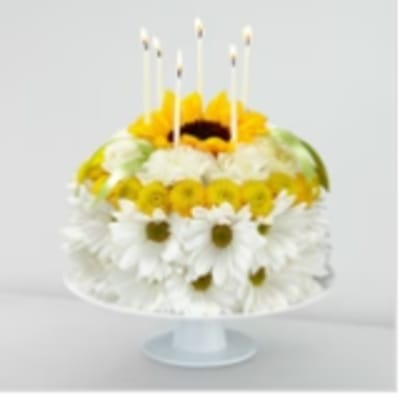 Round floral cake with white daisies and yellow blooms topped by candles