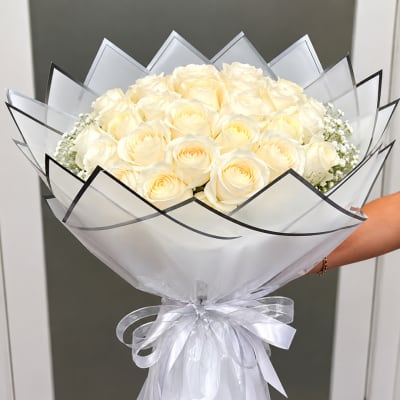 Bouquet of cream roses wrapped in white paper with a silver ribbon