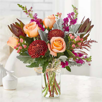 Peach roses and burgundy mums in a clear glass vase