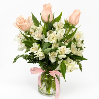 Peach roses and white alstroemeria in a glass vase with a pink ribbon